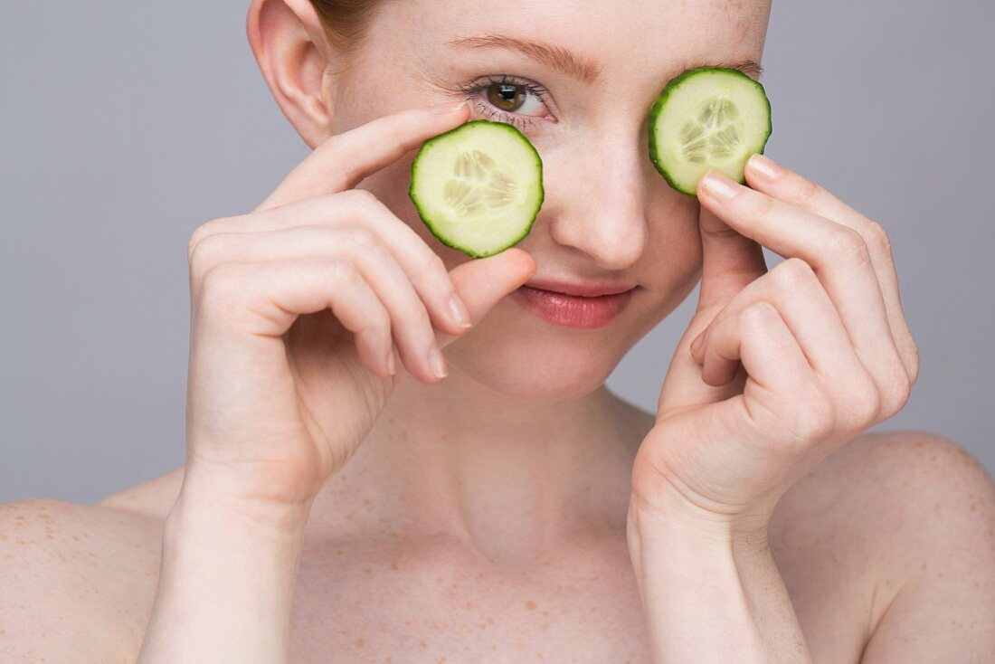 A portrait of a young woman with two slices of cucumber as an eye mask