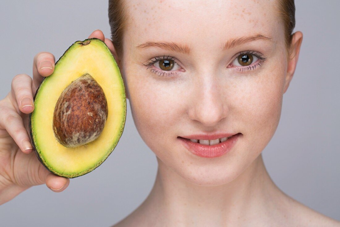 A portrait of a young woman holding an avocado half