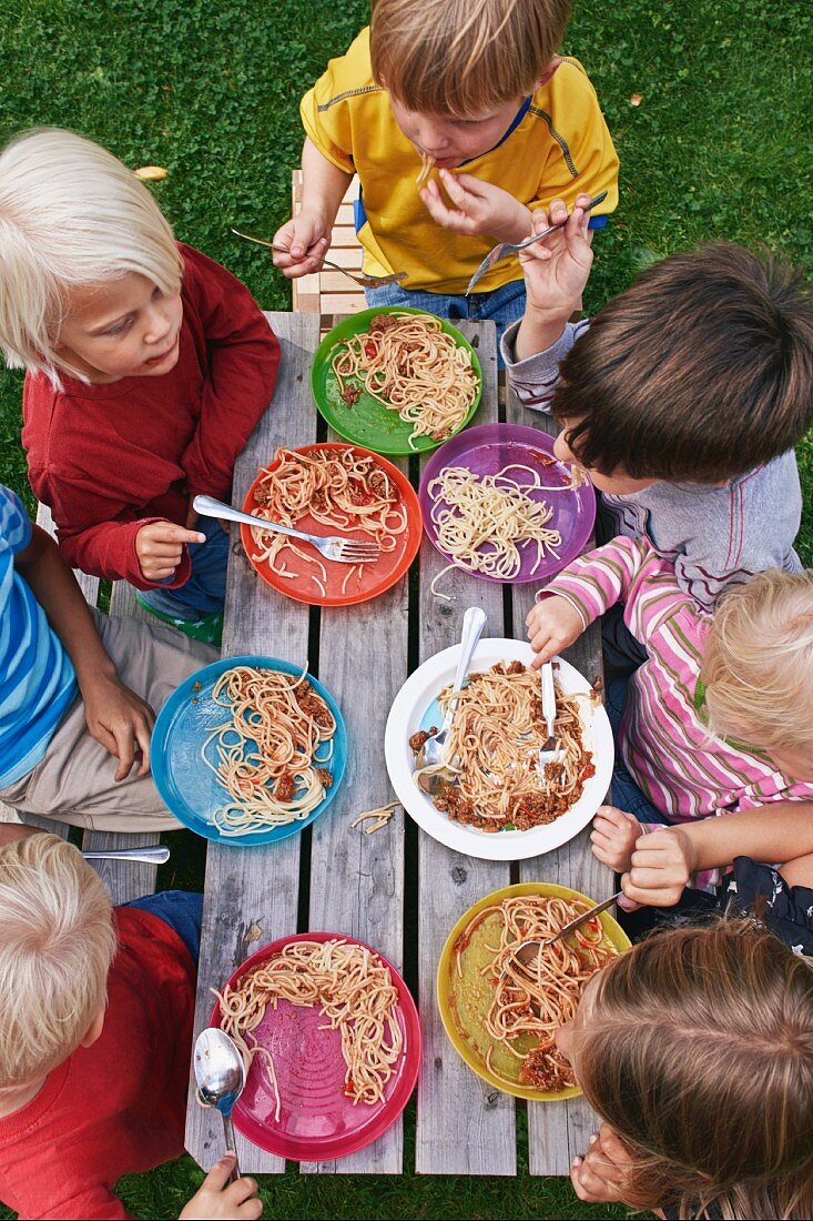Sicht auf Spaghetti essende Kleinkinder an Holztisch im Garten