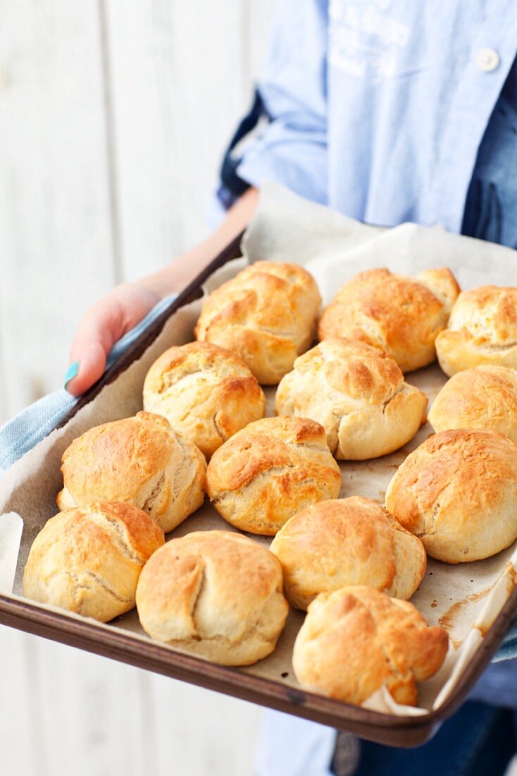 Frau hält Backblech mit frisch gebackenen Hefebrötchen