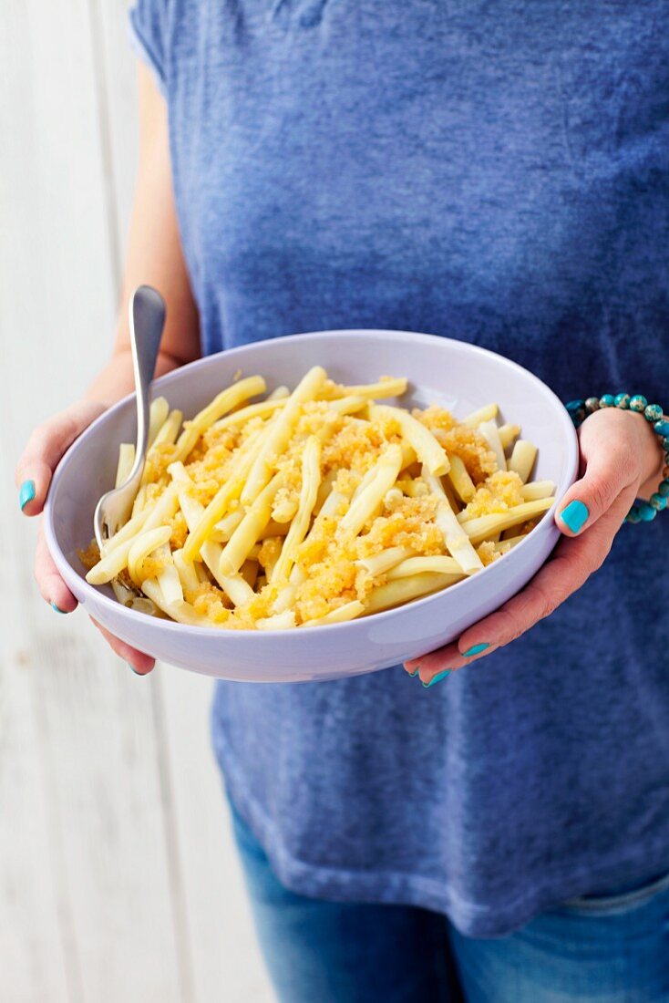 A woman holding a bowl of yellow beans with buttered crumbs