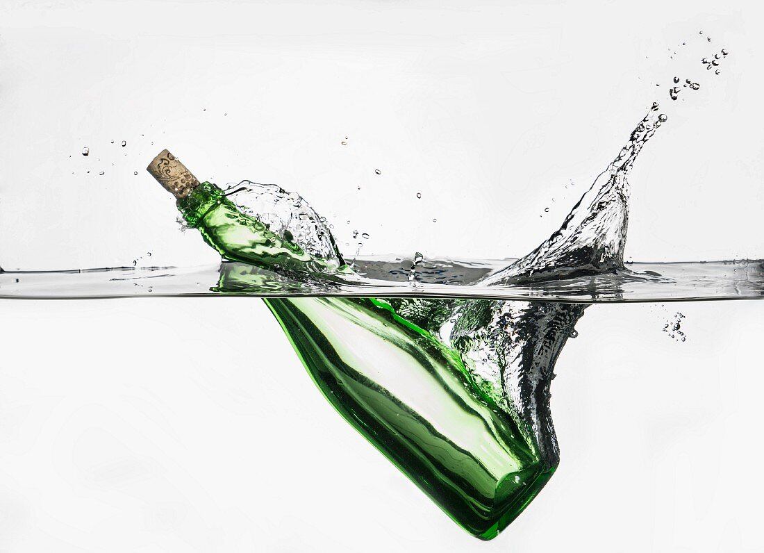 Grüne verkorkte Flasche fällt spritzend in Wasser