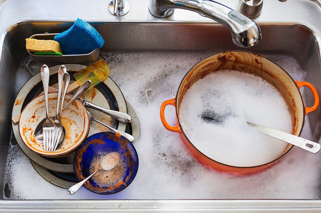 Spülbecken voller schmutzigem Geschirr und Spülwasser
