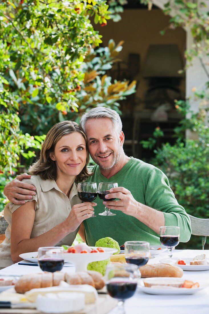 A couple eating together outdoors holding glasses of red wine