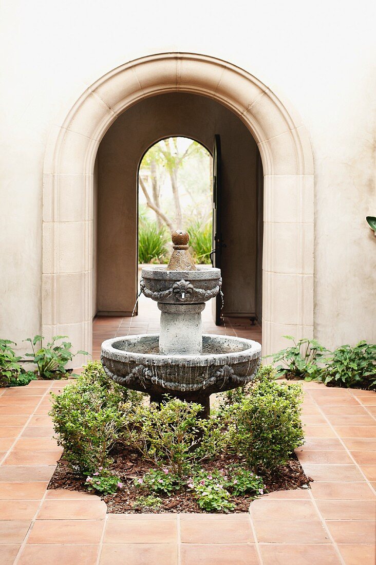 Plants around fountain in courtyard in front of archway