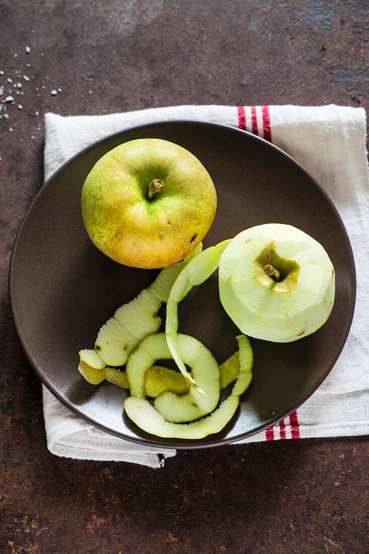 A whole apple and a peeled apple on a plate