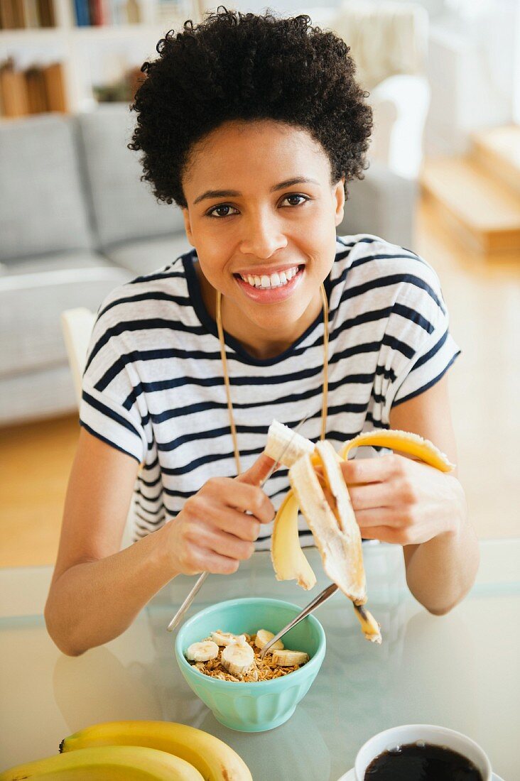 A black woman slicing a banana into a bowl of muesli for breakfast