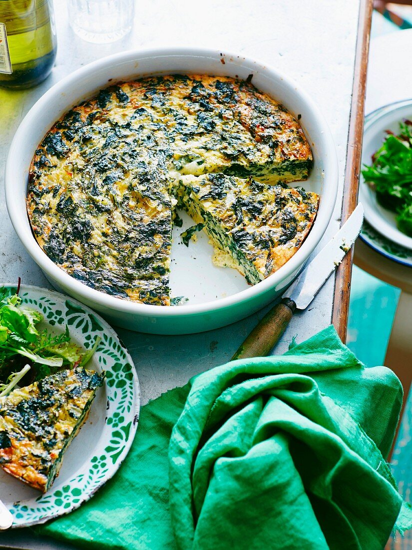 Chard frittata with feta cheese in a baking dish with a slice on a plate
