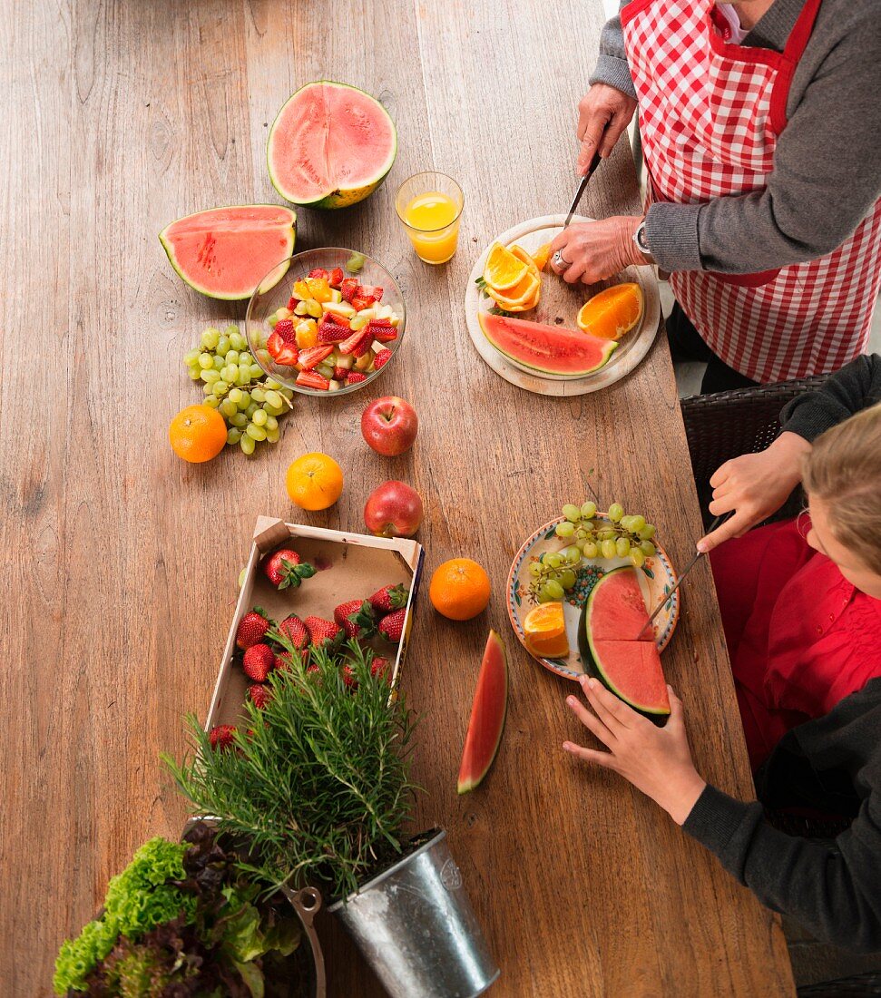 A granddaughter and her grandmother at a kitchen table preparing fruit