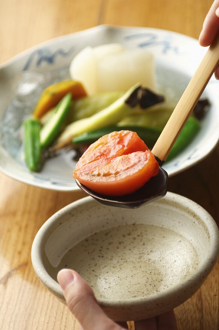 A heart-shaped tomato half from a vegetable dish on a ladle above a bowl