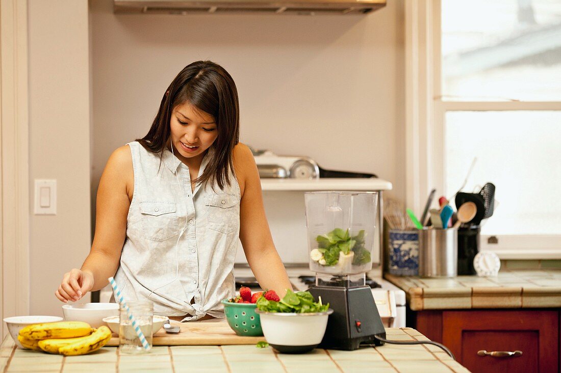 A young woman making green smoothies in a kitchen
