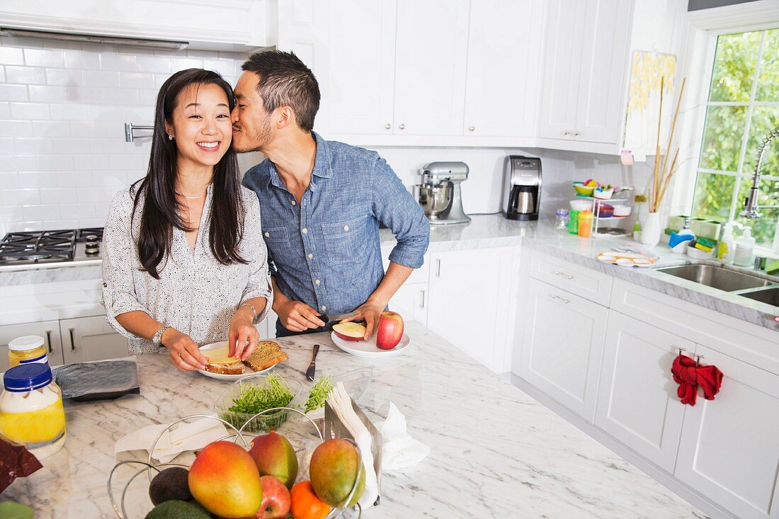 Mann küsst Frau bei Zubereitung eines Sandwiches in Küche