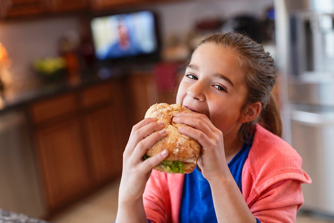 Mädchen in der Küche beißt in grosses Sandwich