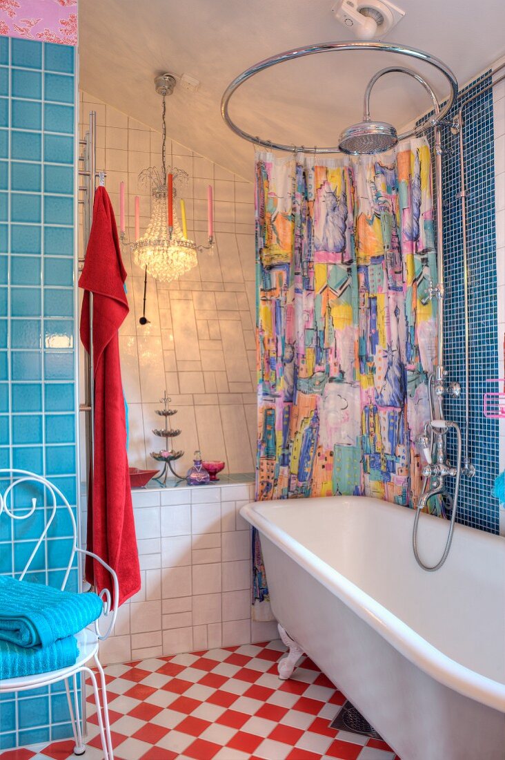 Colourful shower curtain on round curtain rail above retro bathtub; chandeliers and mixture of blue and white tiles in background