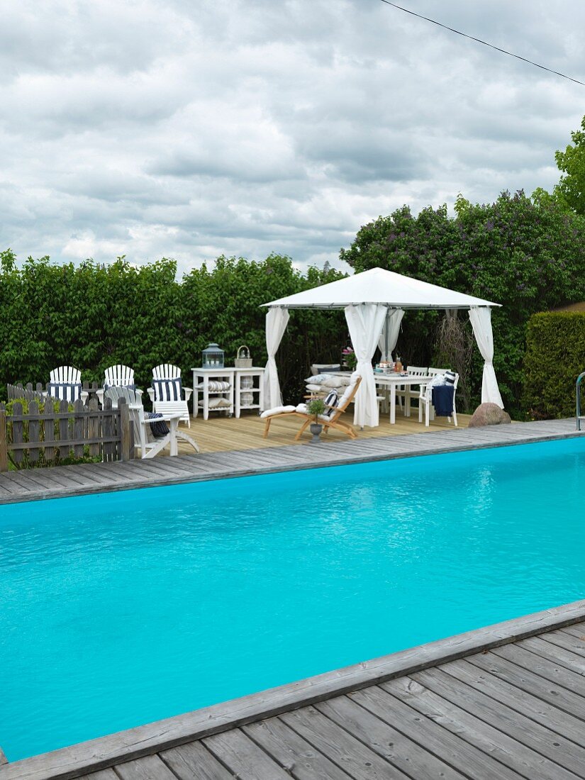 Pool mit Holzeinfassung im Garten, im Hintergrund zeltartiger Pavillon und Sonnenliegen