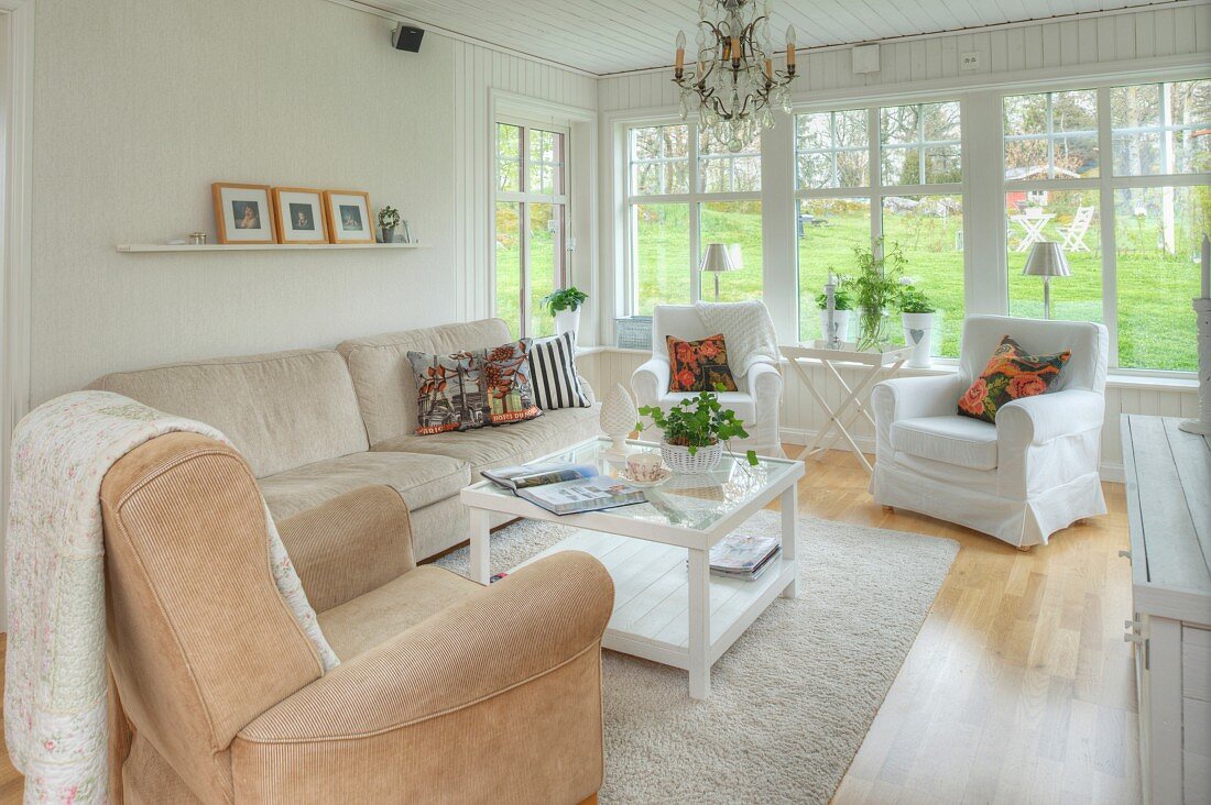 Living room with pale upholstered furniture, crystal chandelier and glass wall