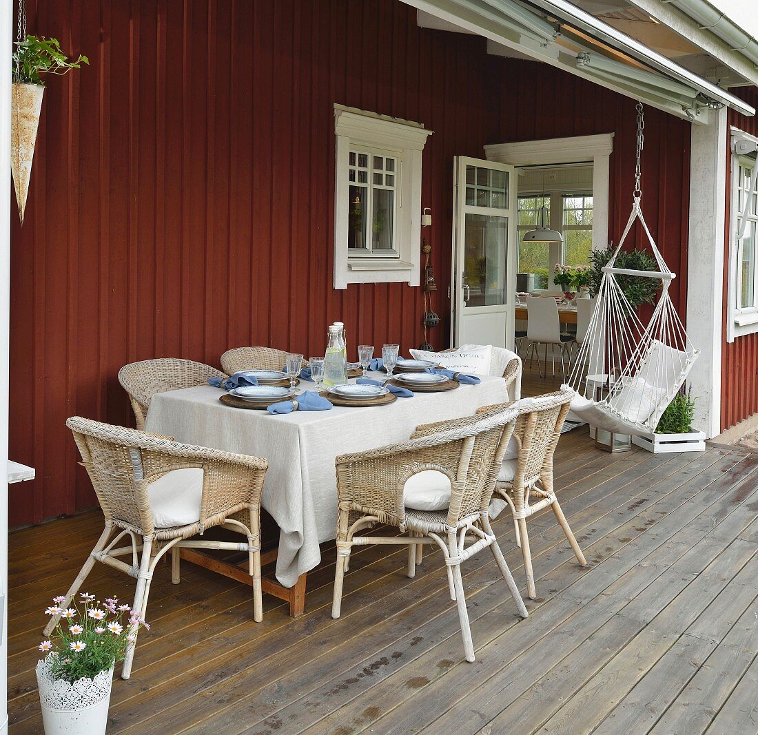 Gedeckter Tisch mit Rattansesseln und Hängestuhl auf der Veranda eines Schwedenhauses