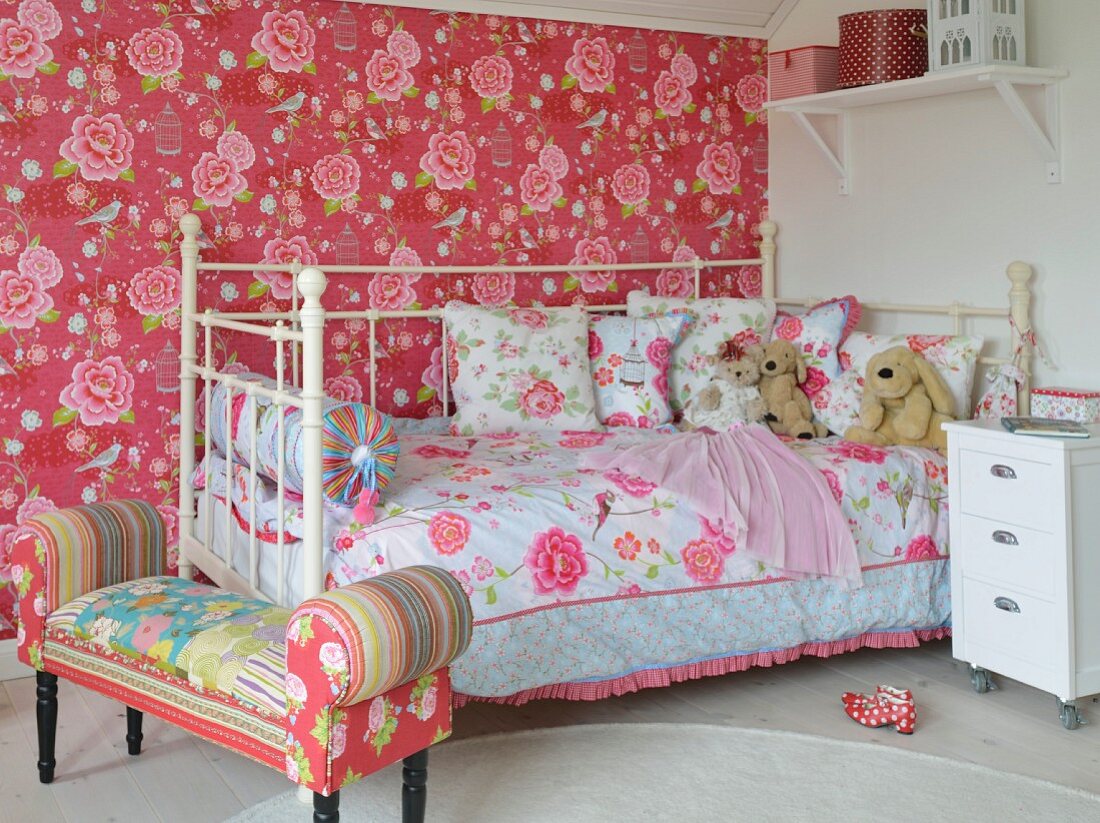 Opulent patterns of roses on wallpaper, bed linen and upholstered bench in girl's bedroom