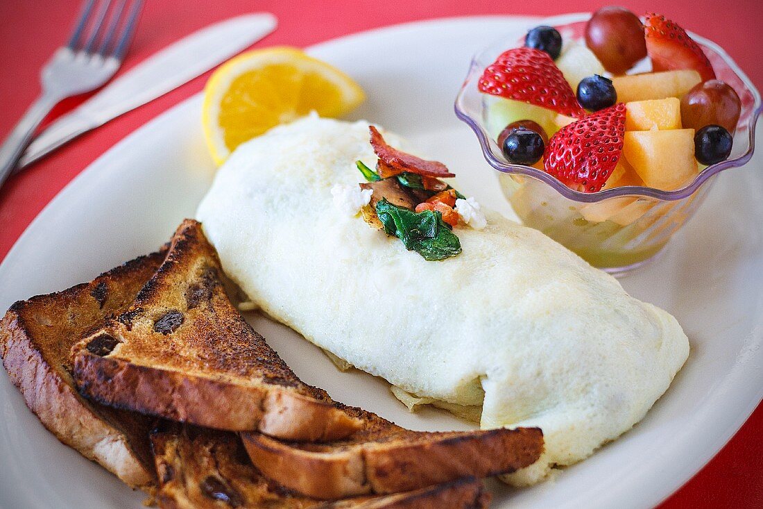 A bacon, spinach and feta omelette served with toast and fruit salad