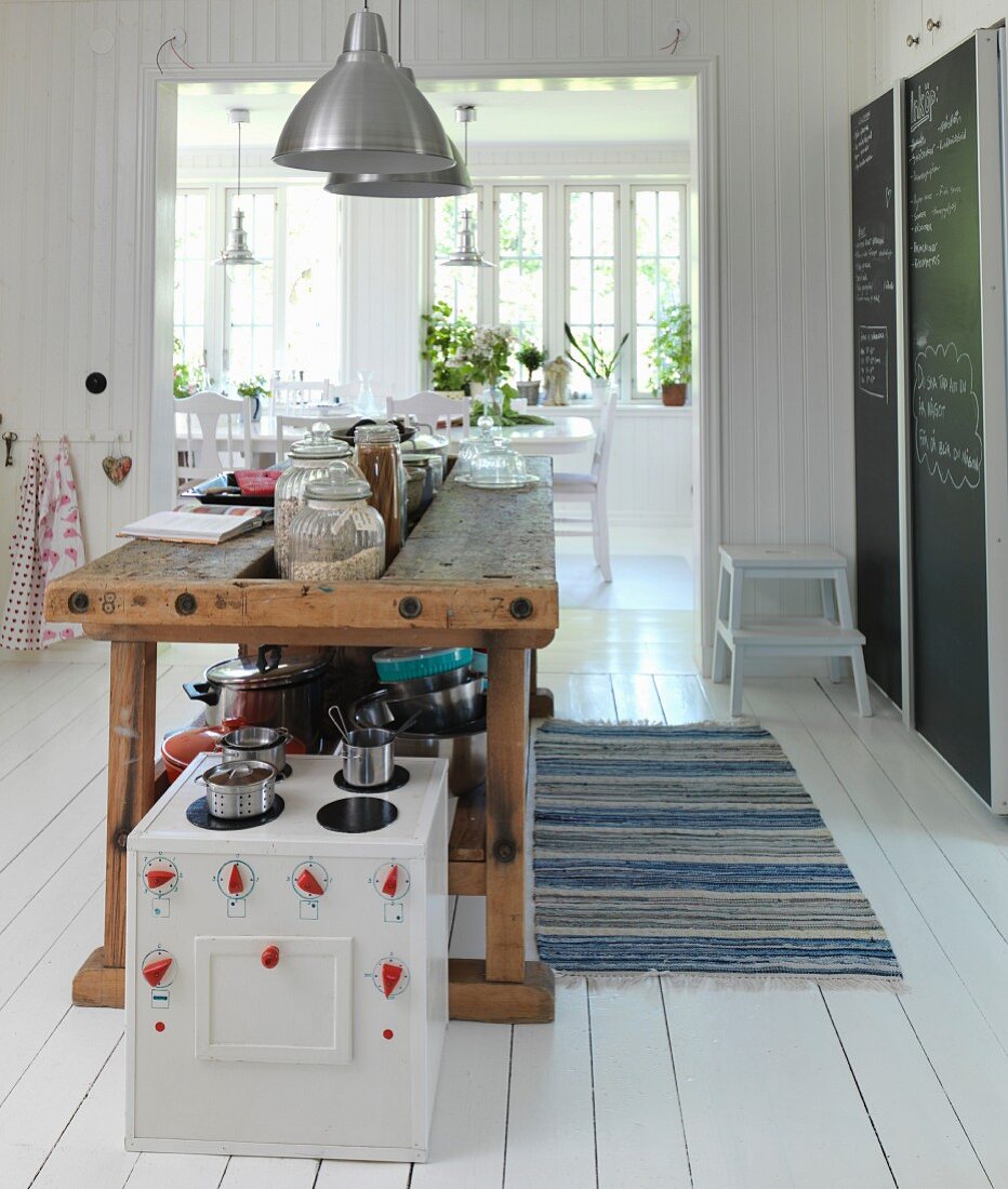 Kinderküche vor alter Hobelbank als Küchentheke in skandinavischer Wohnküche mit weißem Dielenboden