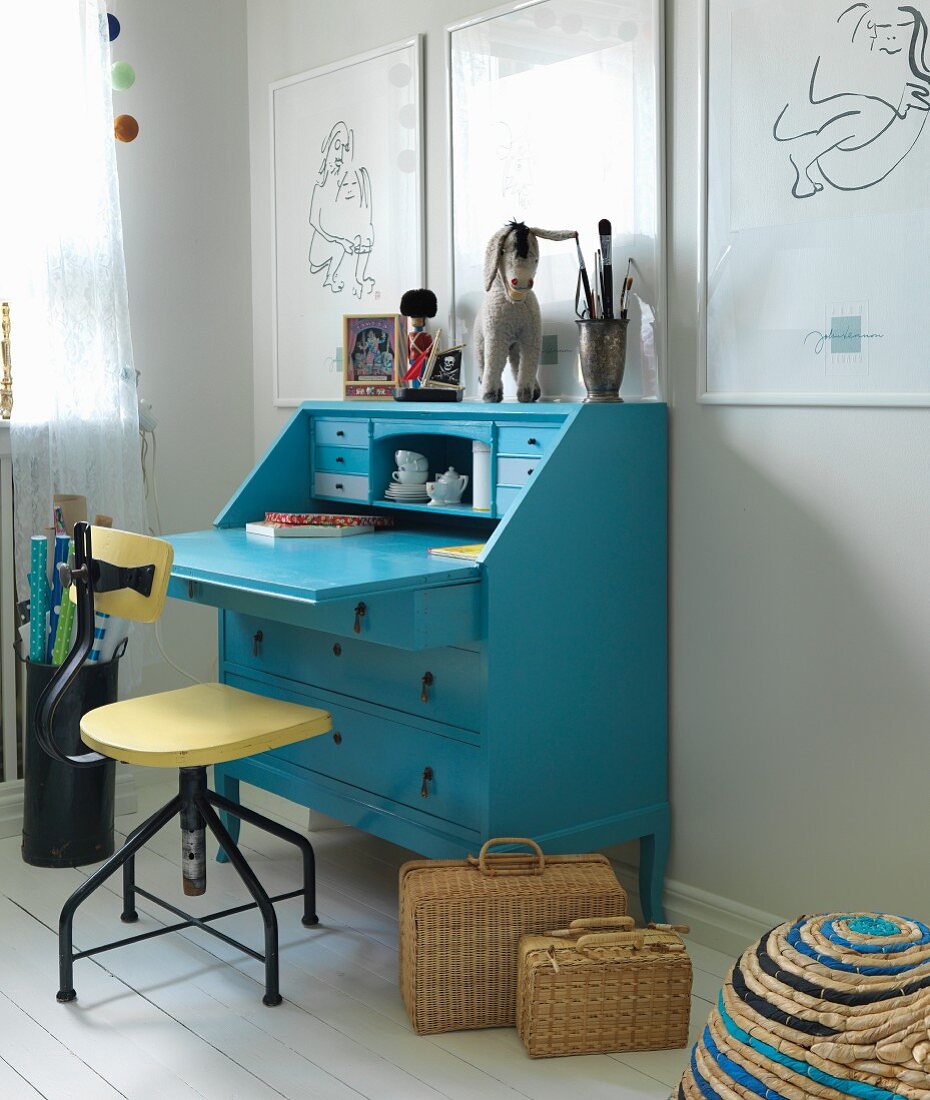 Vintage swivel chair at blue bureau below white-framed drawings on wall