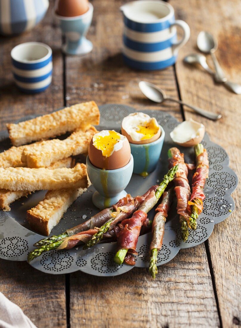 Soft-boiled eggs, asparagus with prosciutto and strips of white bread
