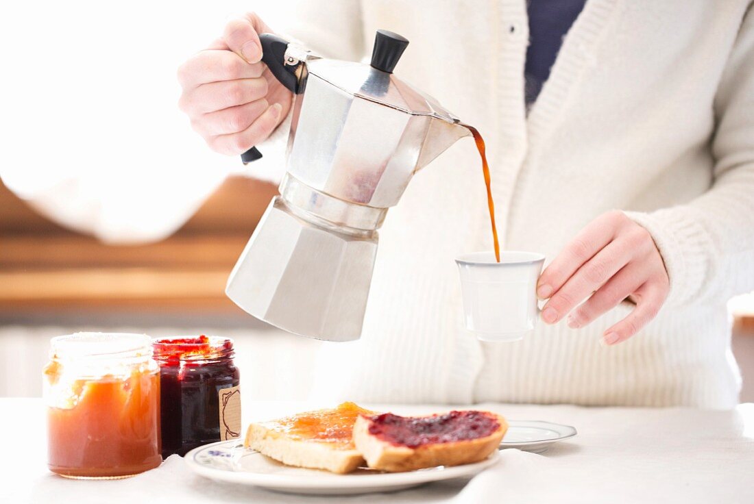 Kaffee wird am Frühstückstisch aus Espressokanne in Tasse gegossen