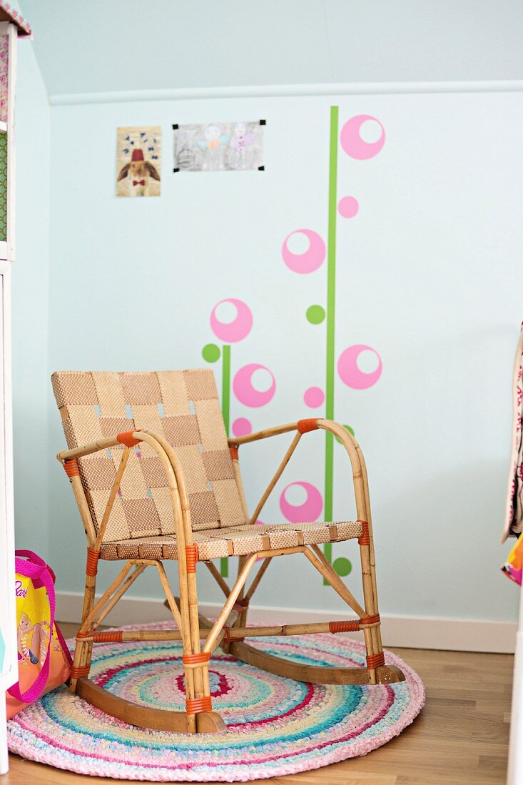 Schaukelstuhl mit Gurtbespannung auf buntem Häkelteppich und Wandtattoo im Kinderzimmer