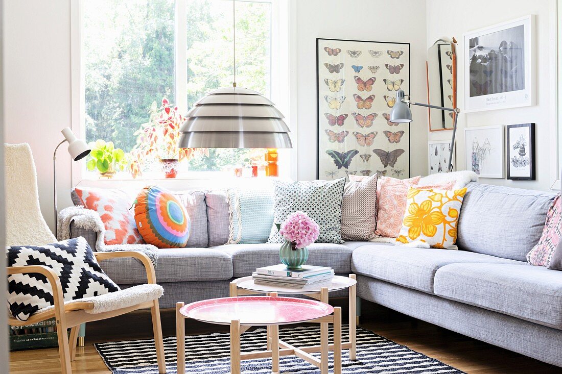 Seating area with patterned, retro scatter cushions on corner sofa, pendant lamp with metal lampshade and Scandinavian side tables