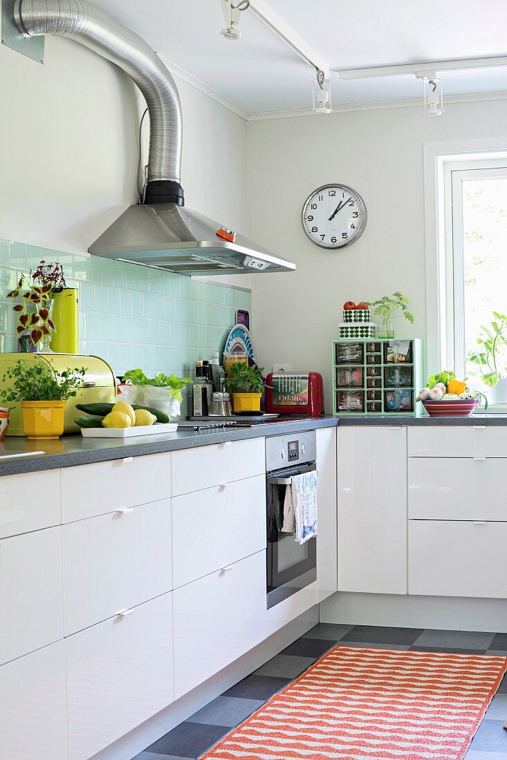 Simple fitted kitchen with retro utensils on grey worksurface and orange rug on grey chequered floor