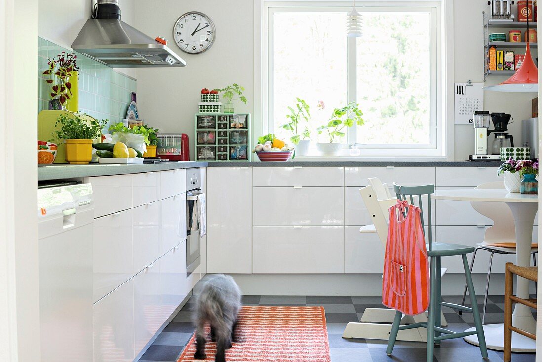 Base units with glossy white fronts in bright, retro kitchen-dining room with various chairs