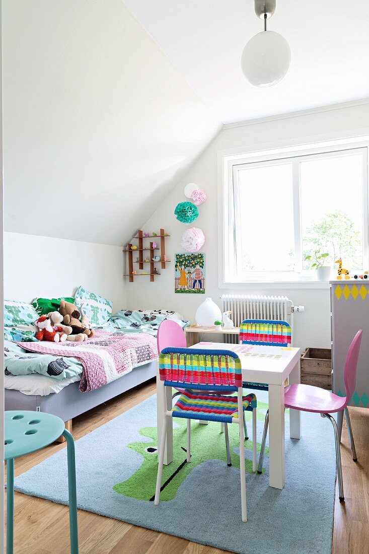 Spieltisch mit bunten Stühlen auf Tiermotiv-Teppich und Bett mit Patchworkdecke im Kinderzimmer