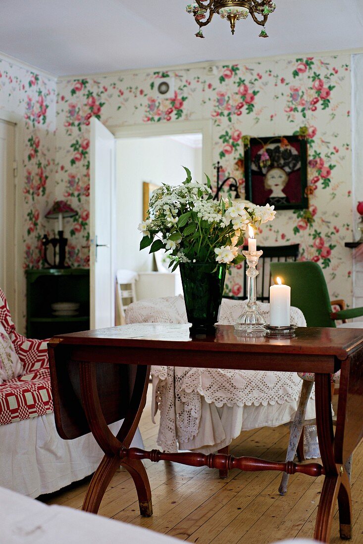 White bouquet in vase on antique wooden table in rustic interior with floral wallpaper