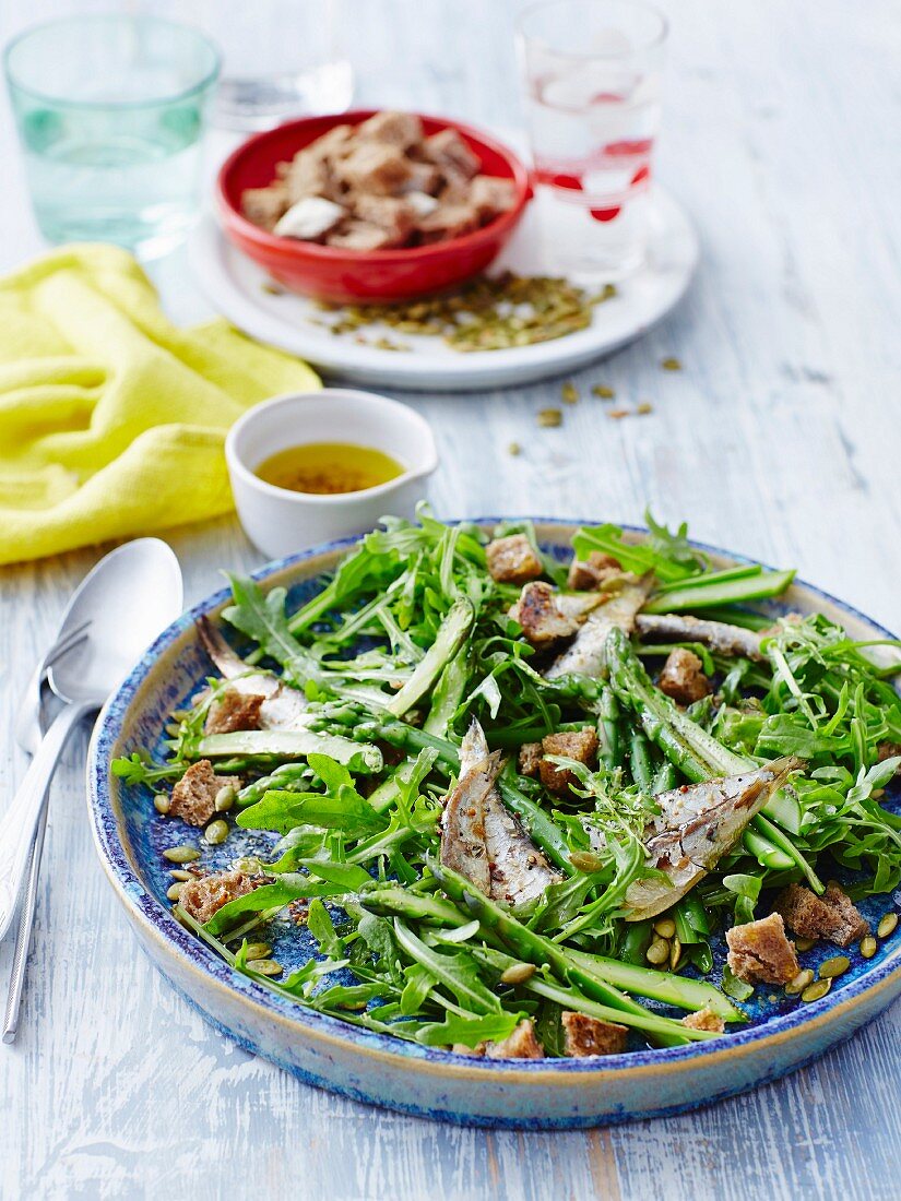 Salat aus Rucola und grünem Spargel mit Sardinen und Croûtons