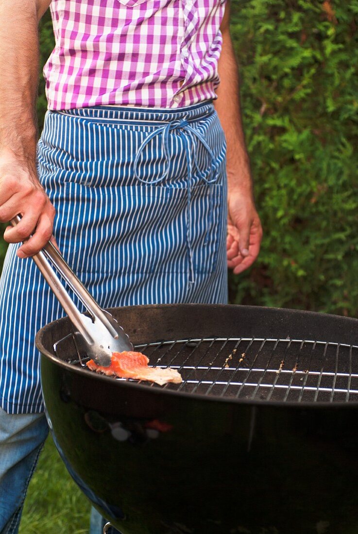 Mann mit Schürze grillt Lachsforellen Filet im Garten