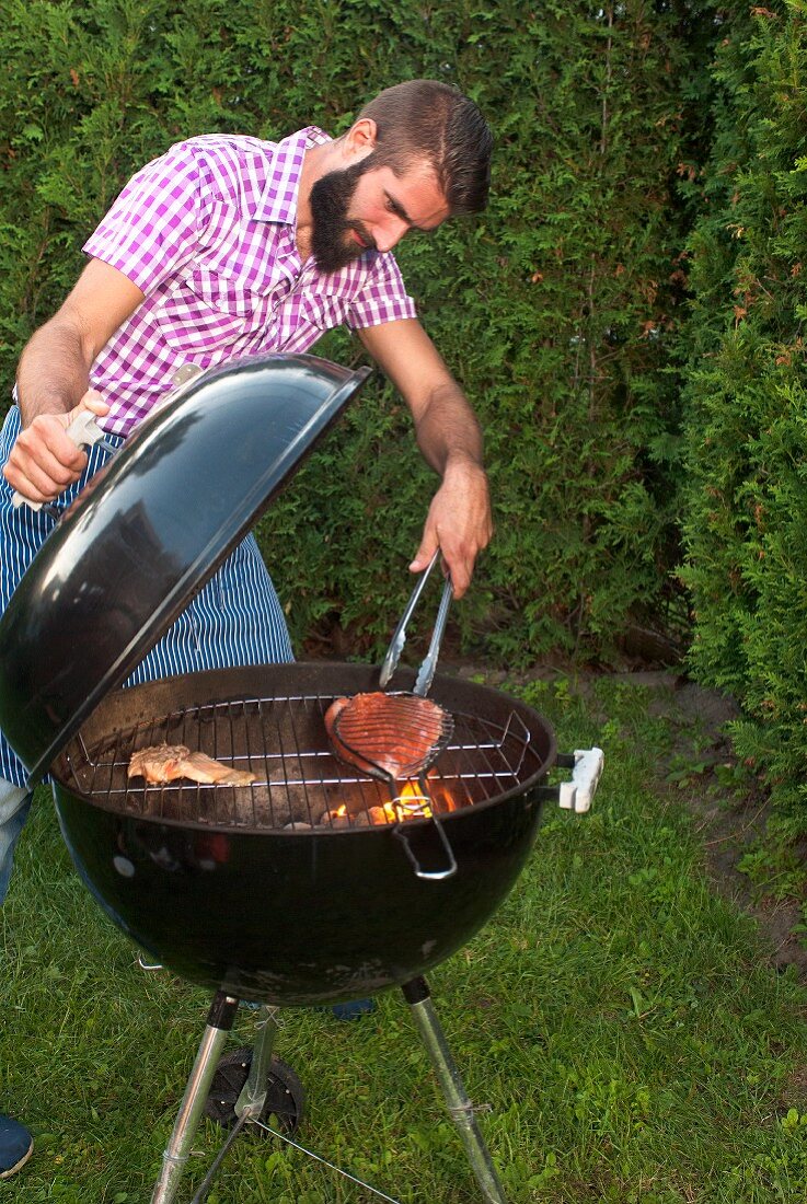 A young man returning salmon trout on a kettle barbecue