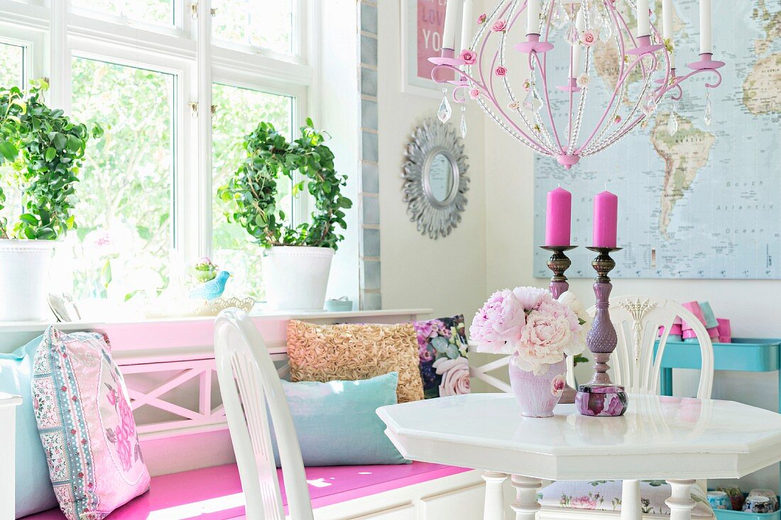 Vintage-style, white dining area with vase of flowers and candlesticks on table and bench below window