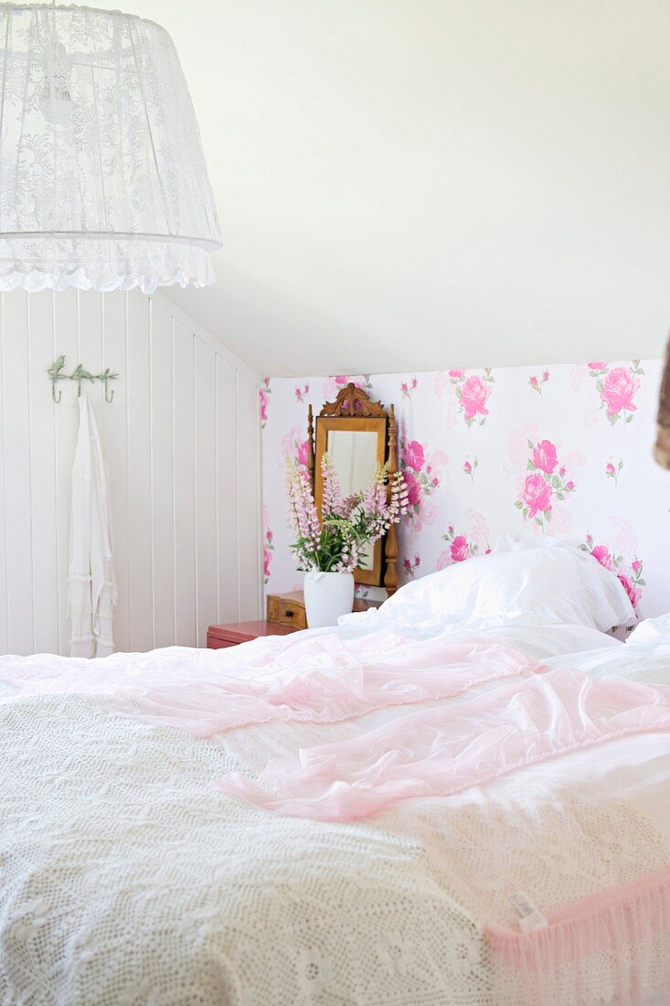 Doppelbett mit rosa Spitzendecke, vor Blumentapete in nostalgischem Stil