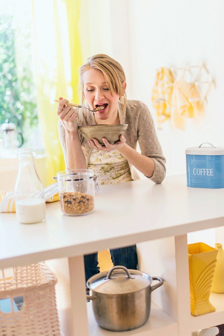 A blonde woman eating muesli in a kitchen