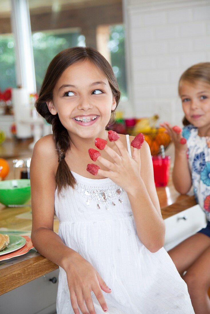 Zwei Schwestern mit Himbeeren auf ihren Fingern in der Küche