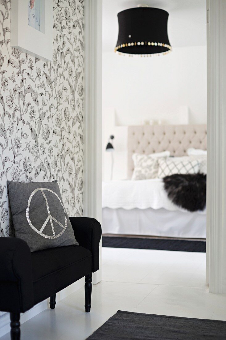 Cushion with CND symbol on black couch against floral, black and white wallpaper outside elegant bedroom with black lampshade