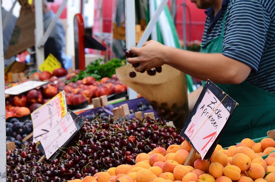 A fruit seller filling a paper bag with cherries at a market stand