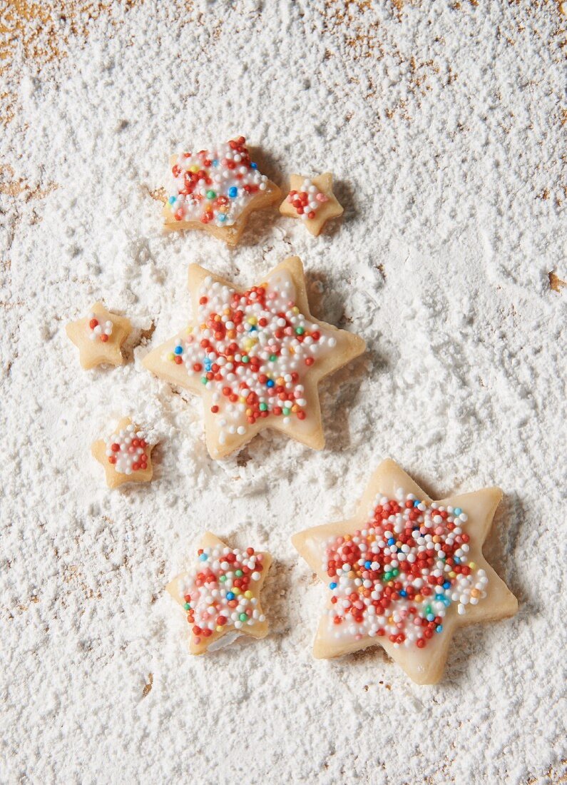 Star biscuits with coloured sprinkles on a sugared wooden board