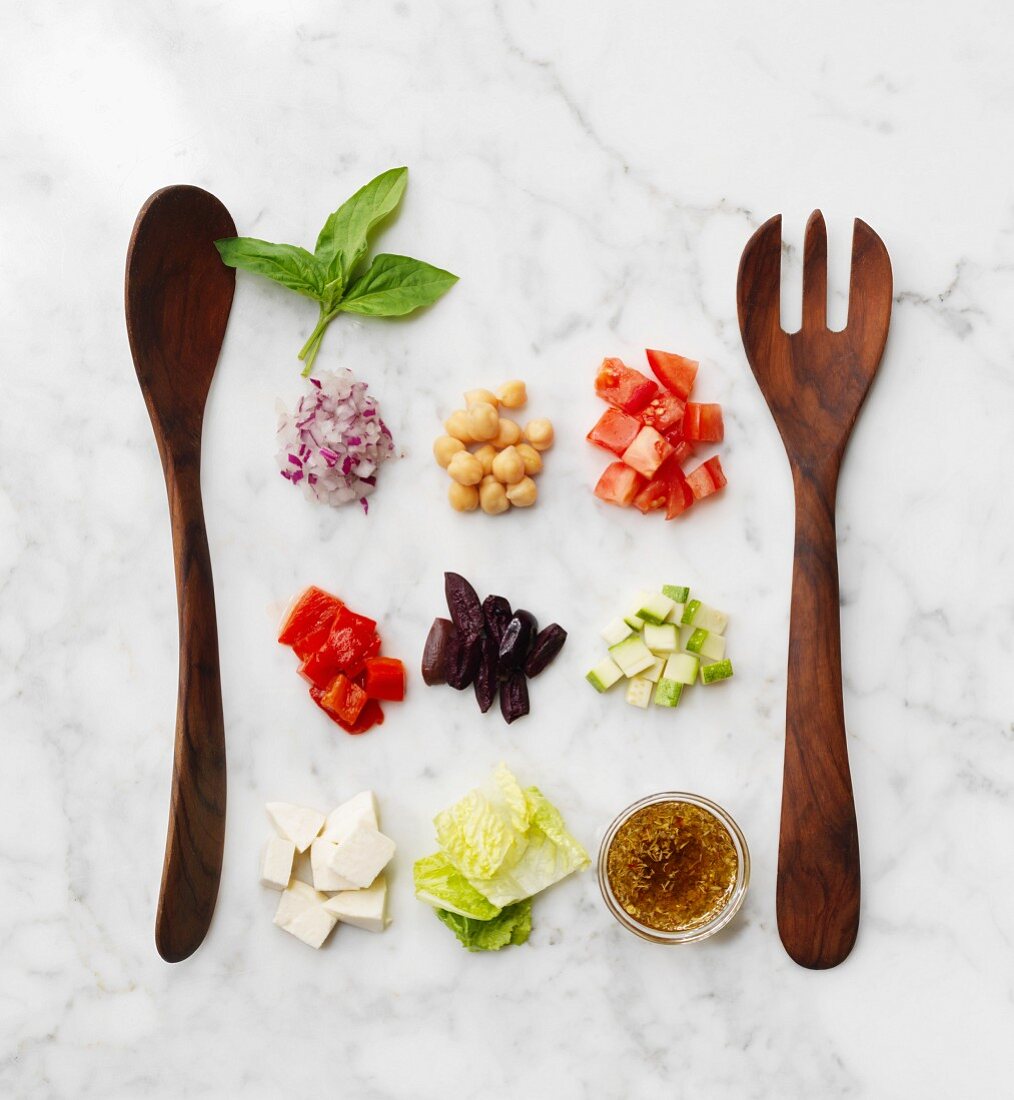Chopped salad ingredients with salad servers on a marble surface