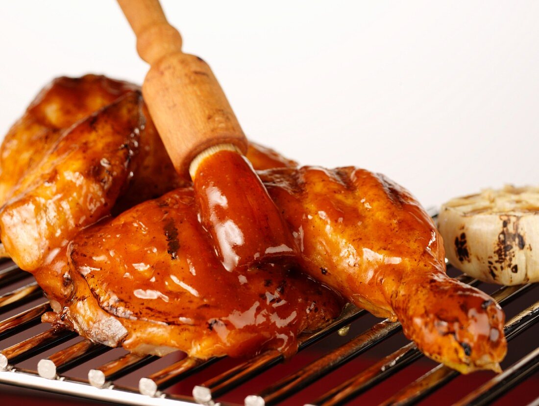 Grilled chicken being brushed with barbecue sauce