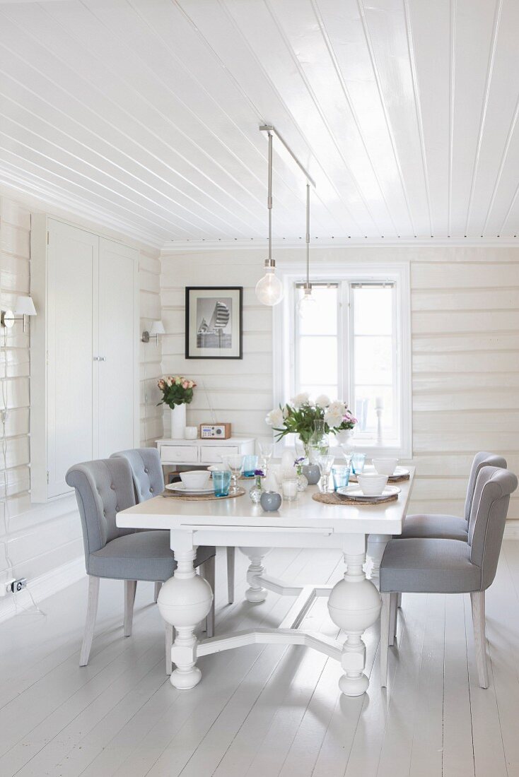 White table with carved feet and chairs upholstered in pale grey in white, wood-clad dining room