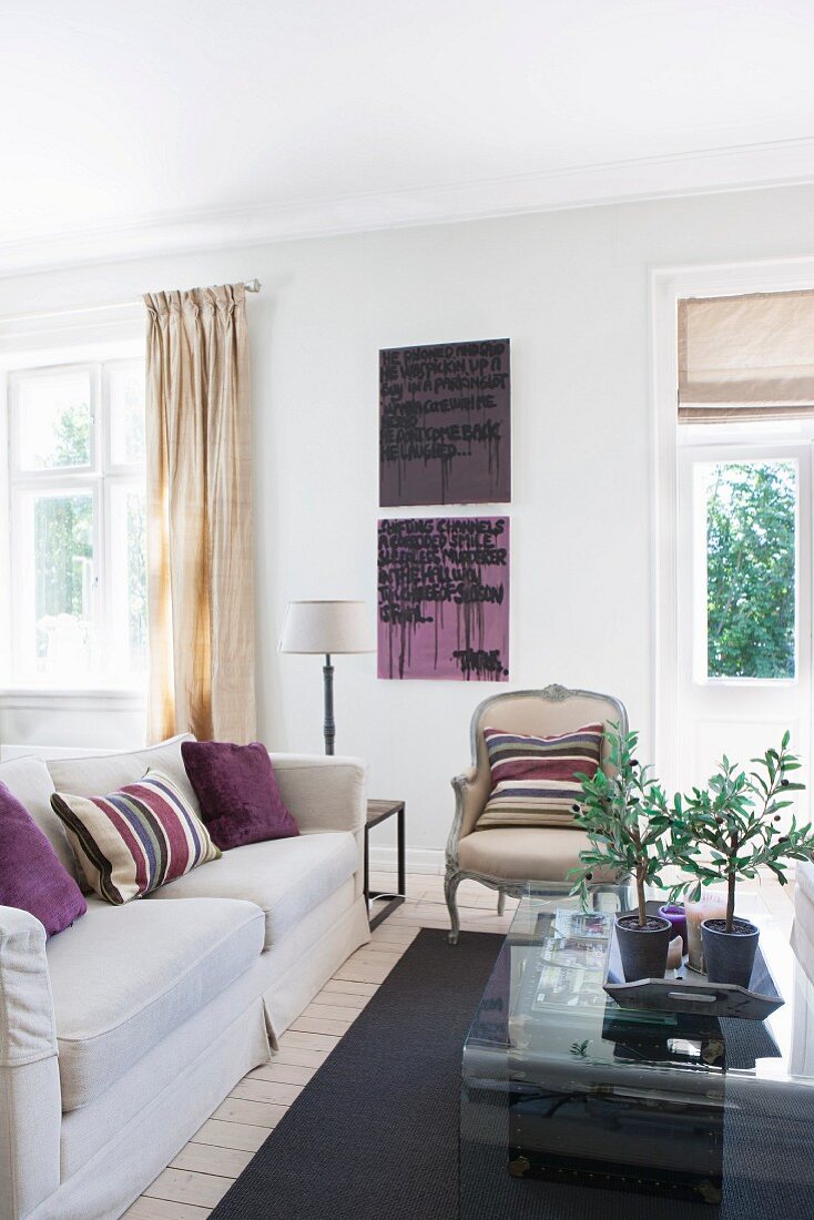 Pale sofa with scatter cushions and Rococo armchair around curved glass coffee table