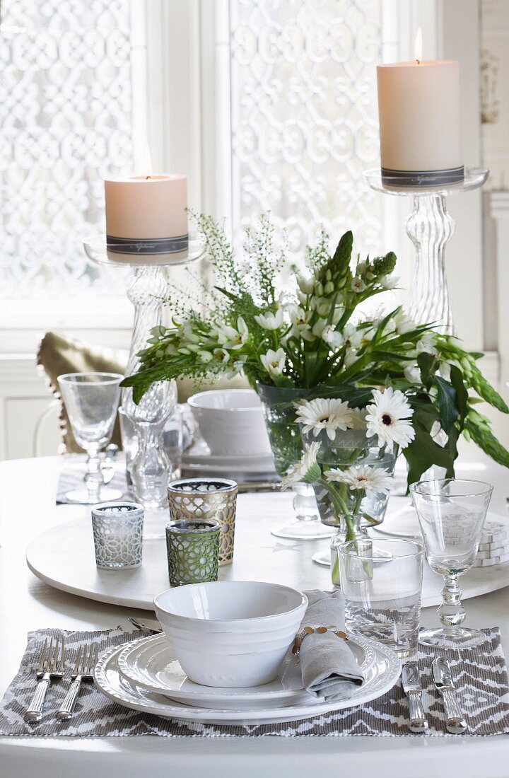 Place setting with white plates and patterned place mat; tealight holders and vases of flowers on lazy Susan