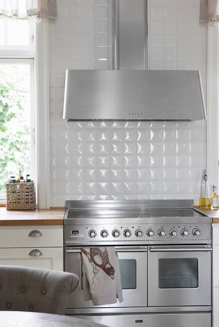 Stainless steel cooker below extractor hood against white-tiled wall