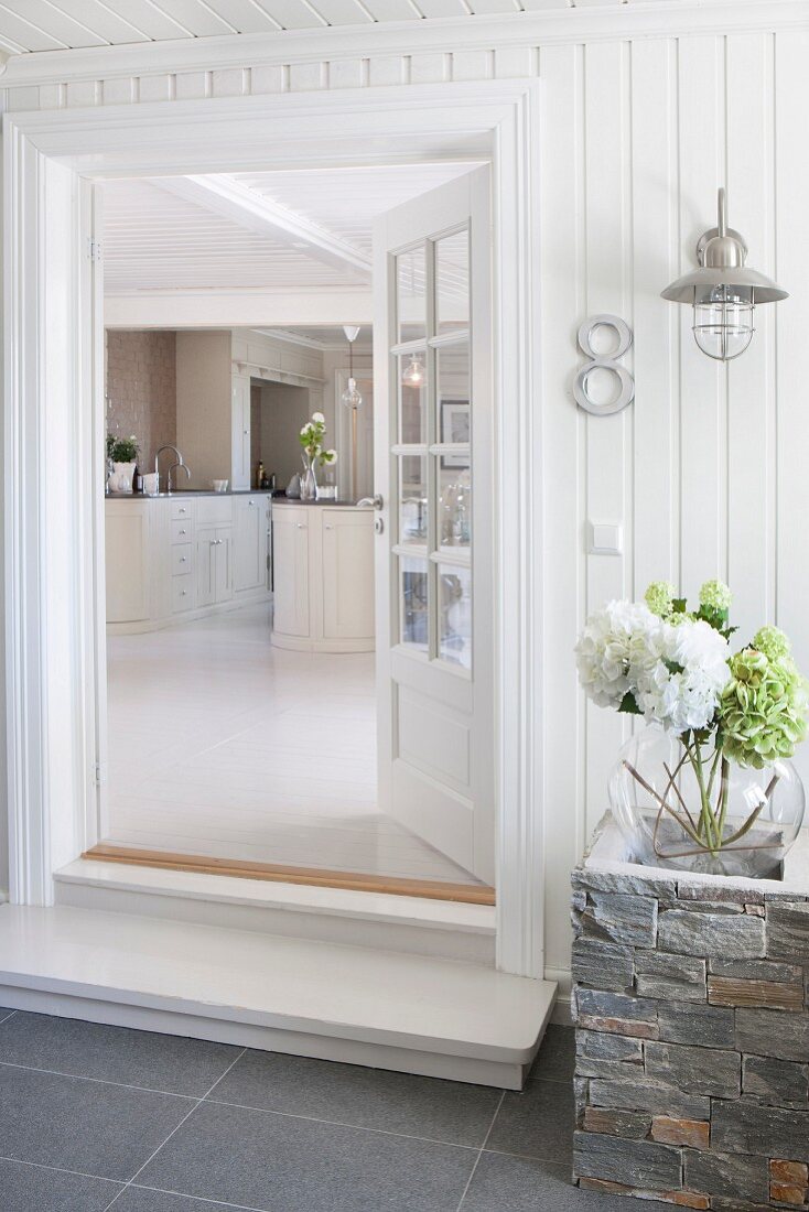 Open front door of white wooden house with view into kitchen area in interior